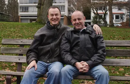 Robert and his partner Mitchell sitting close on a park bench in leather jackets, autumn leaves on the grass, Vancouver 2008.